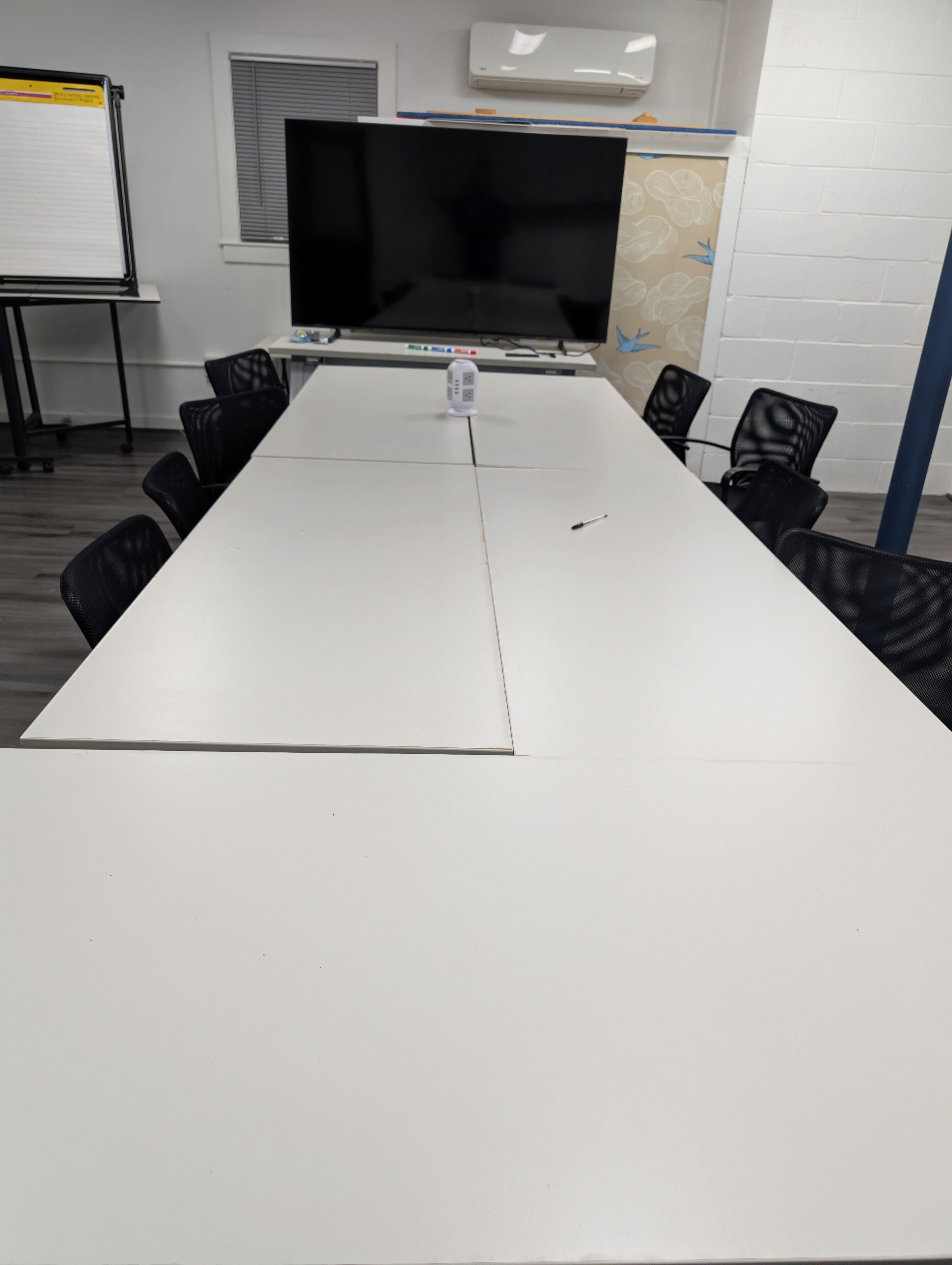 A conference room with a long white table, black chairs, a large flat-screen TV, and a whiteboard.