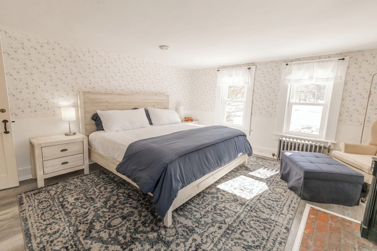 Un dormitorio con cama, mesitas de noche, un banco y una ventana con cortinas.