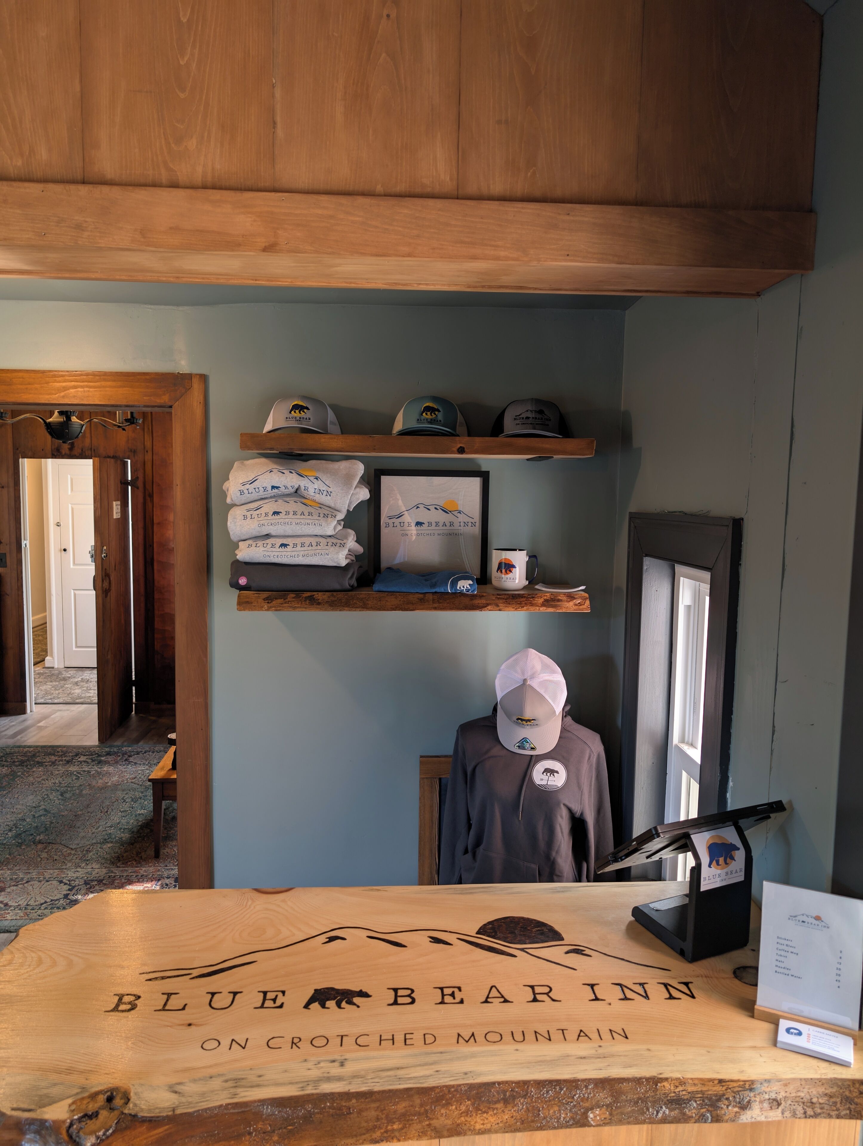 A wooden reception desk with the Blue Bear Inn logo, a display of hats, and a framed sign.