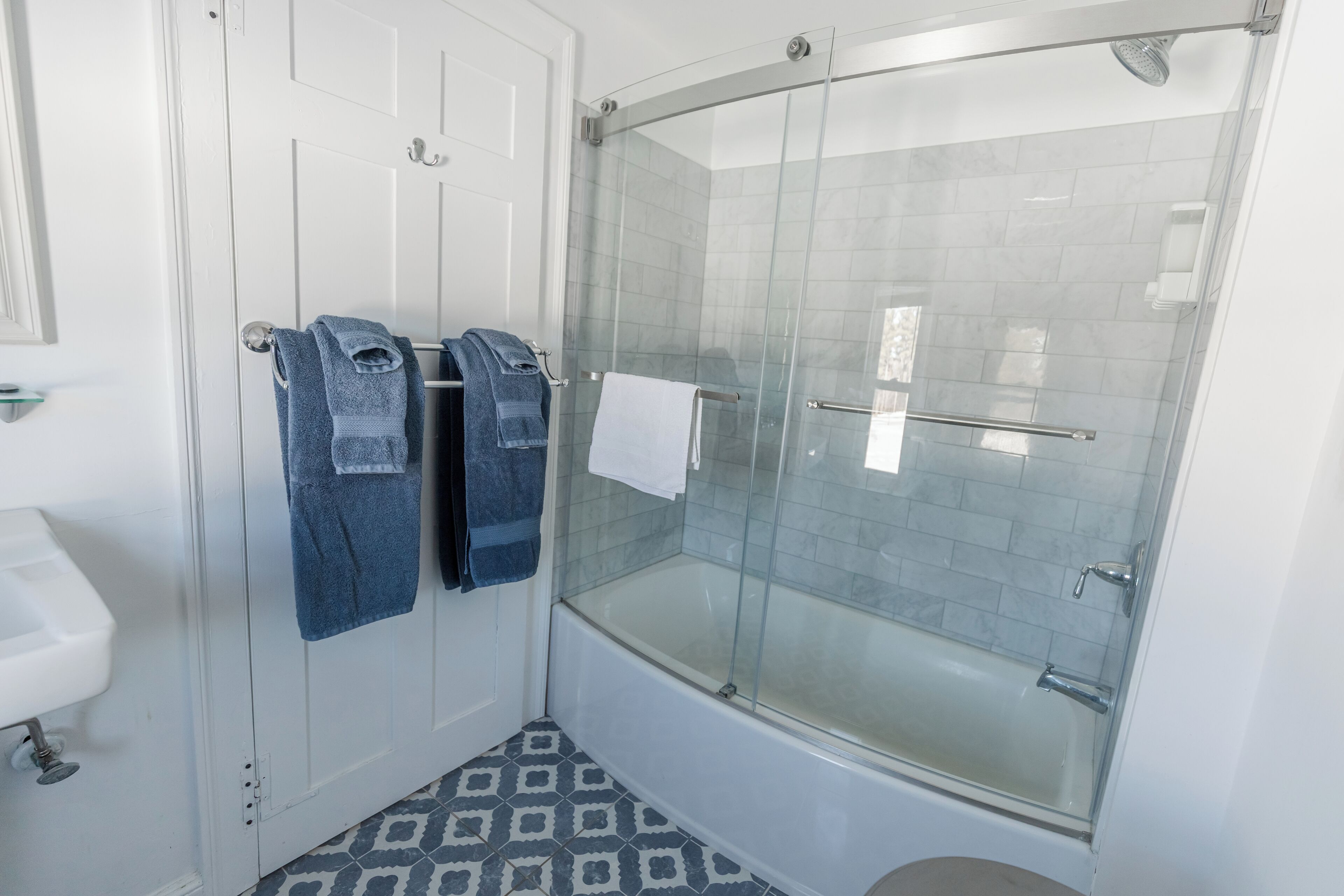 Un baño moderno con ducha acristalada, lavamanos blanco y baldosas de piso estampadas.