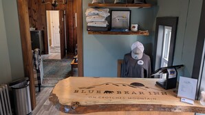 A reception desk with a wooden top labeled "Blue Bear Inn on Crooked Mountain," a display of hats, and a mannequin wearing a cap. - Blue Bear Inn (Francestown)