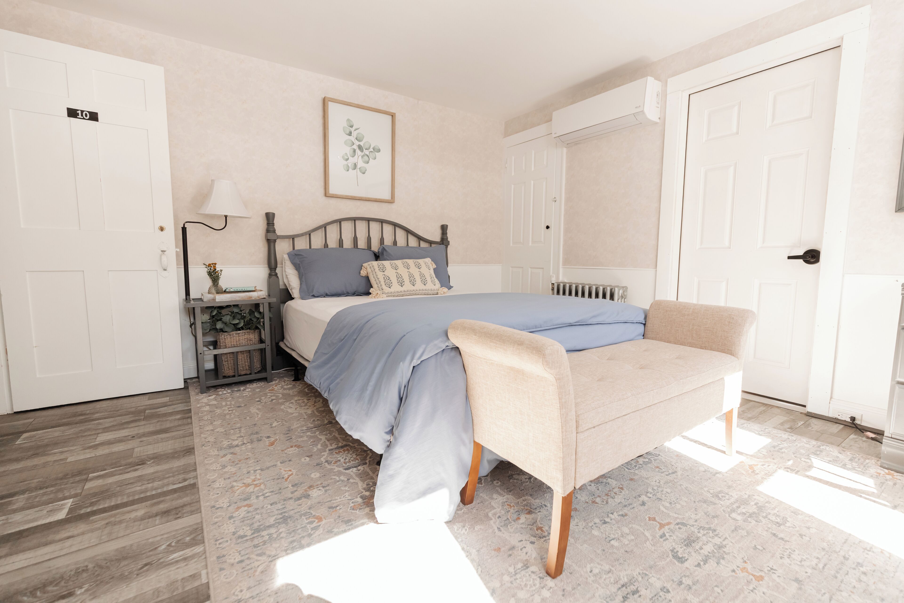 A bedroom with a bed, a bench, a nightstand, a lamp, and a framed picture on the wall.
