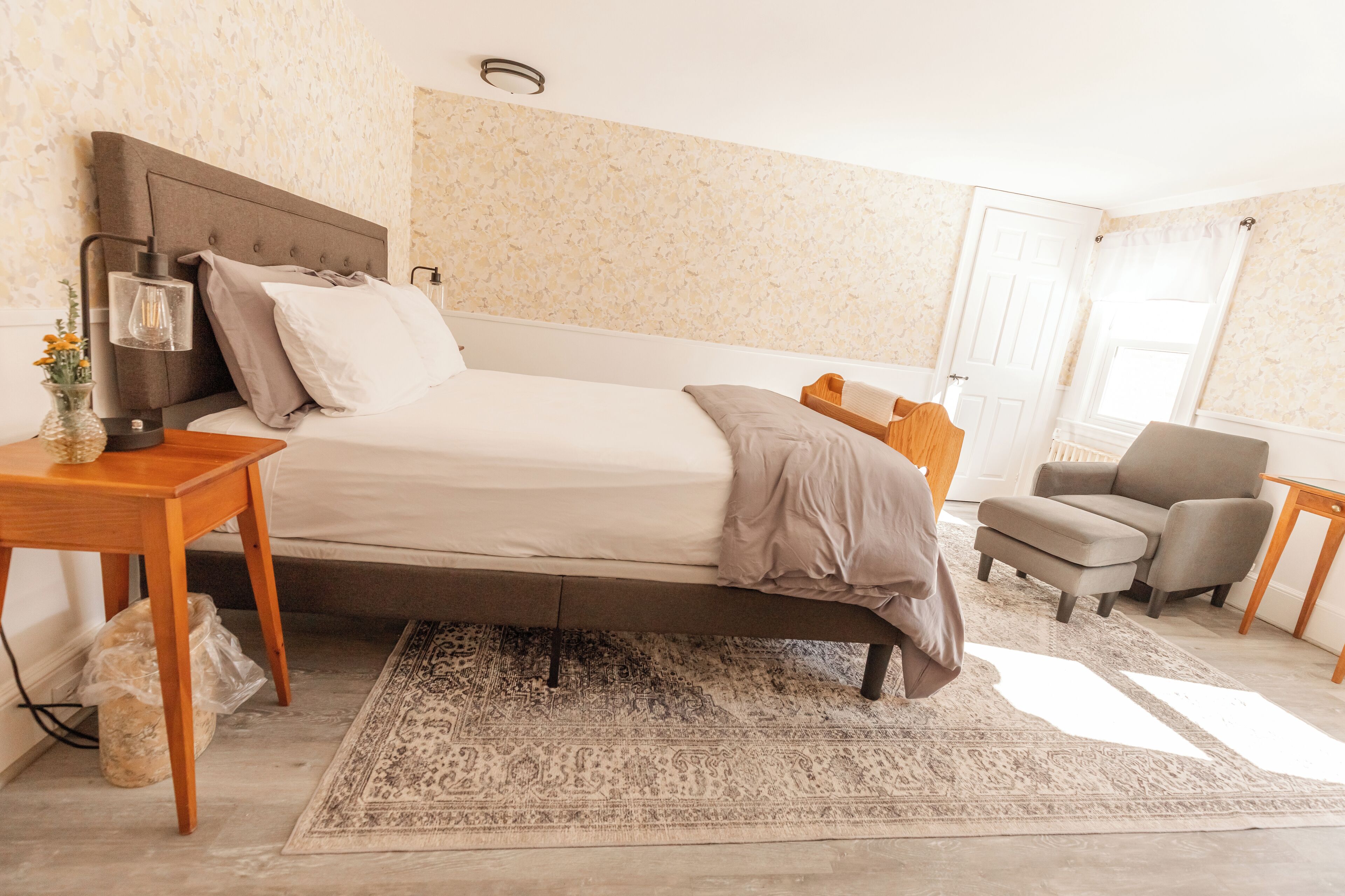 A bedroom with a bed, bedside table, lamp, chair, and a rug.