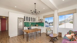 A spacious kitchen with a dining area, a purple sofa, and a view of a town through large windows. - Amazing 2 Bedroom Apartment With Mountain Views on Kloof Street (Cape Town)