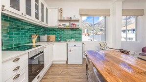 A kitchen with white cabinets, green tiled backsplash, wooden countertop, and a view of mountains through the window. - Amazing 2 Bedroom Apartment With Mountain Views on Kloof Street (Cape Town)