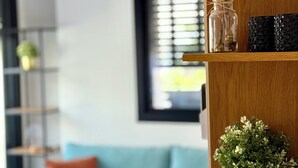 A modern living room with a teal sofa, a wooden shelf with decorative items, and a window with blinds. - Lovely 1-bedroom apartment in The best location (Tel Aviv-Yafo)