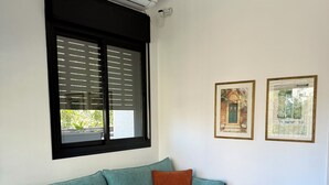 A teal sofa with a brown pillow, a small wooden table with two cups, and a black-framed picture on the wall. - Lovely 1-bedroom apartment in The best location (Tel Aviv-Yafo)
