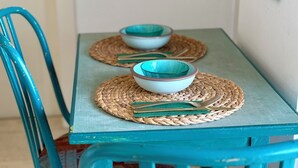 A small dining table with two bowls and chopsticks on woven placemats, surrounded by turquoise chairs. - Lovely 1-bedroom apartment in The best location (Tel Aviv-Yafo)