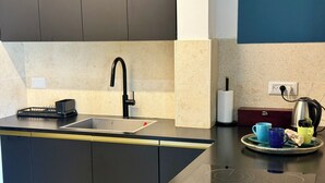 A modern kitchen with a black faucet, a kettle, and a tray with cups and a box of tissues. - Lovely 1-bedroom apartment in The best location (Tel Aviv-Yafo)