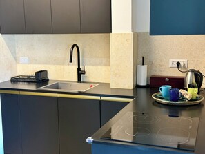 Una cocina moderna con un grifo negro, una tetera y una bandeja con tazas y una caja de pañuelos.
