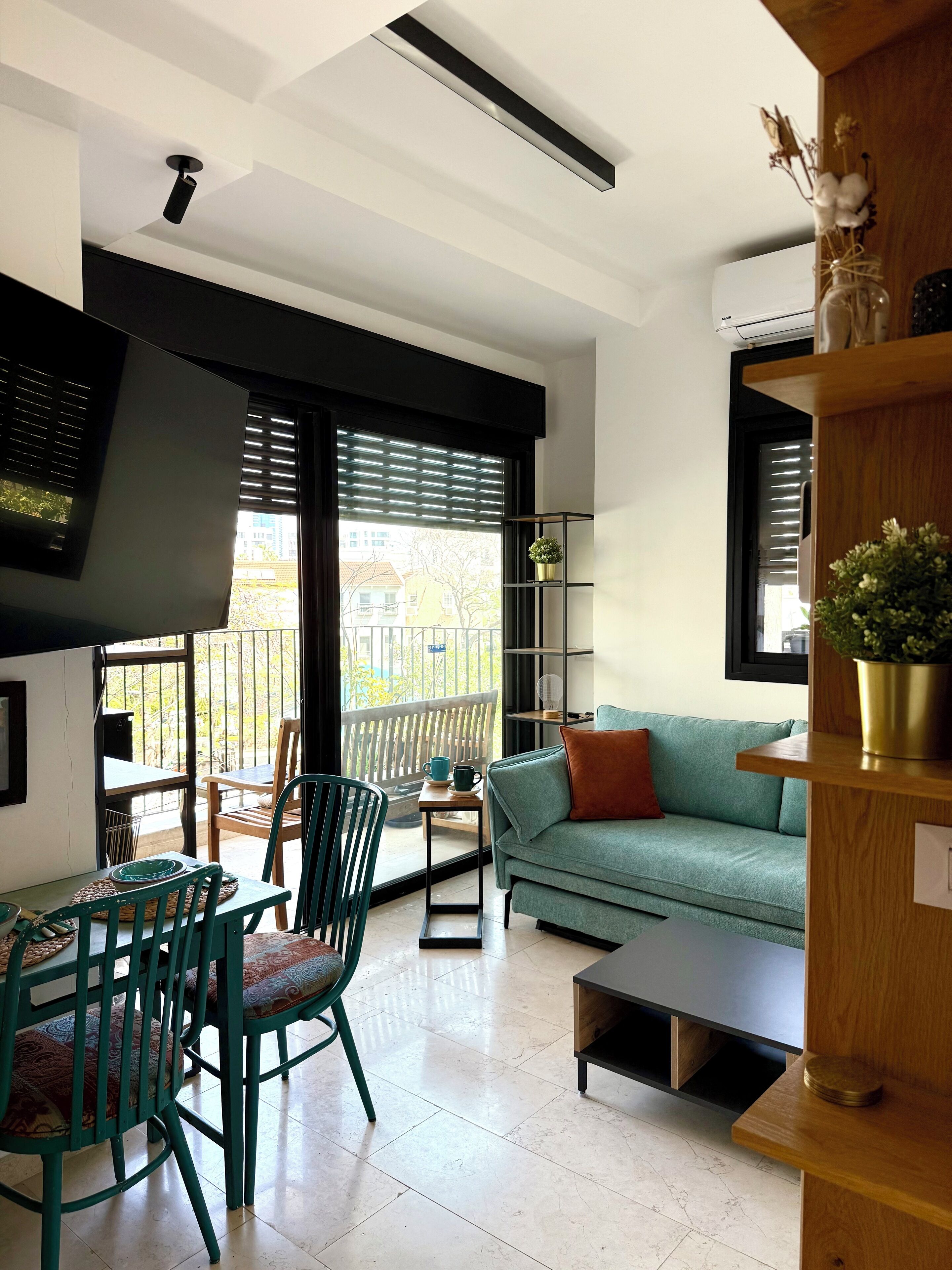A modern living room with a teal sofa, a wooden coffee table, and a dining area with green chairs and a small table.
