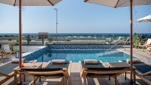A poolside area with lounge chairs and umbrellas, overlooking a clear blue sea. - Calla Luxury Seafront Suites (Rethymno)