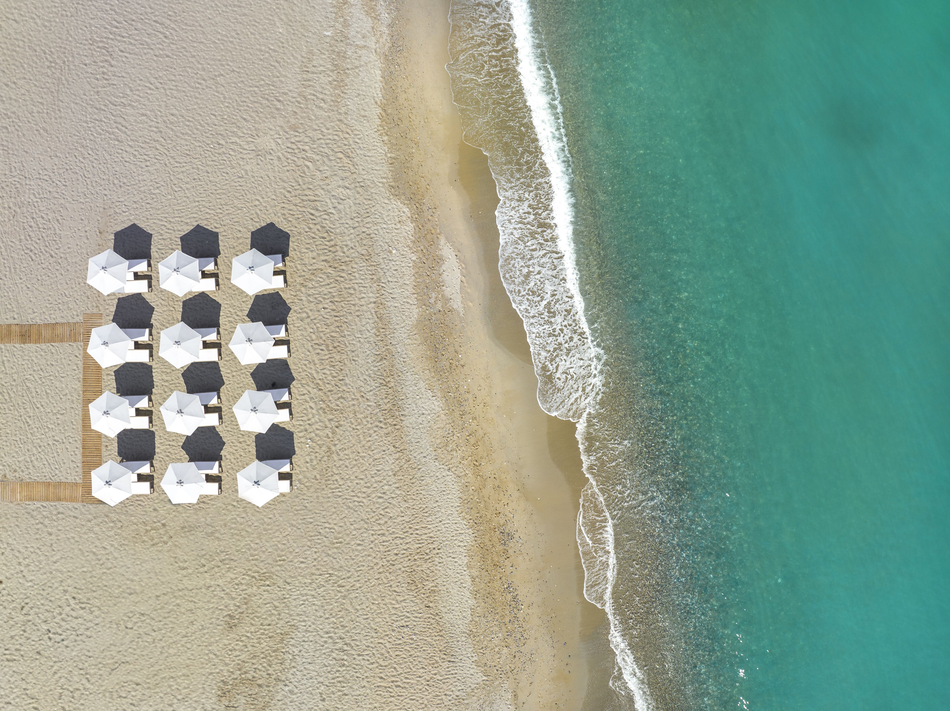 Vista aérea de una playa con hileras de sombrillas y sillas de playa.