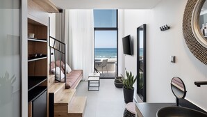 A modern living room with a view of the ocean, a flat-screen TV mounted on the wall, and a dining area with a small table and chairs. - Calla Luxury Seafront Suites (Rethymno)