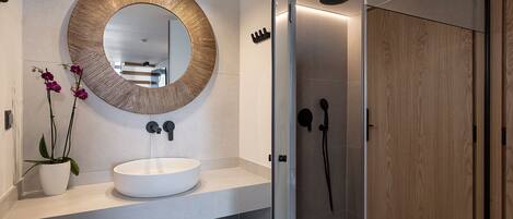 A modern bathroom with a round mirror, white sink, and a shower area.