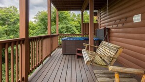 Une terrasse en bois avec un jacuzzi, une chaise suspendue et une petite table.