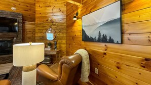 L’intérieur d’un chalet en bois, avec un fauteuil inclinable en cuir, un téléviseur fixé au mur, une lampe, un tableau encadré et une cheminée.