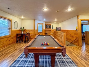 A pool table in a room with wooden walls and a plaid rug.
