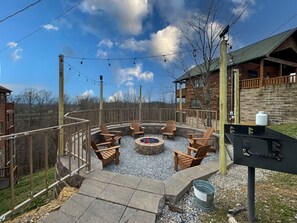 A circular outdoor seating area with fire pit, wooden chairs, and a grill station.