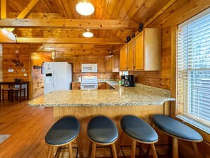 Interior de una cabaña de madera con cocina, taburetes de bar y zona de comedor.