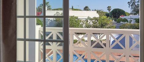 Une vue depuis un balcon donnant sur une piscine, avec des balustrades blanches et un ciel bleu dégagé.