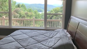 A bedroom with a large window, a bed with a grey quilt, and a wooden headboard. - Amazing view from the Family Lake Retreat (Murphy)