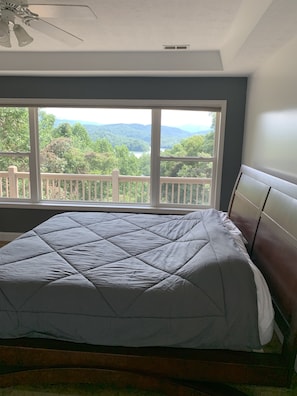 A bedroom with a large window, a bed with a grey quilt, and a wooden headboard.