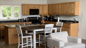 A modern kitchen with wooden cabinets, a central island, and a dining area with white chairs. - Amazing view from the Family Lake Retreat (Murphy)