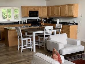 A modern kitchen with wooden cabinets, a central island, and a dining area with white chairs.