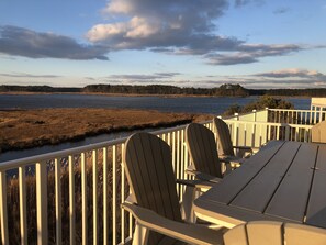 En træterrasse med Adirondack-stole med udsigt over vand og en skovklædt kystlinje.
