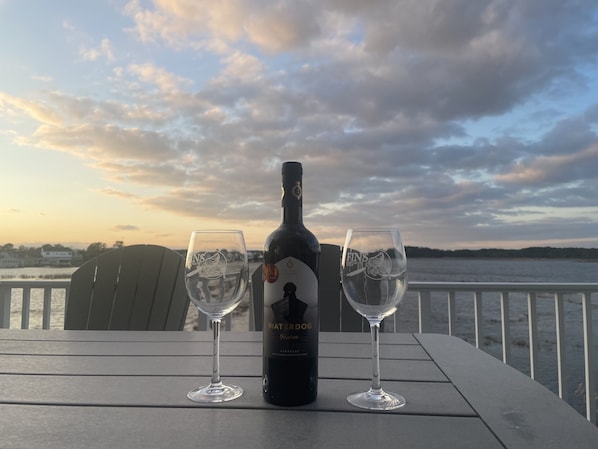 Una botella de vino y dos copas sobre una mesa con vista al agua y al cielo.