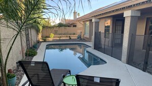 A swimming pool with two chairs and a table, surrounded by a garden with plants and a building in the background. - North Phoenix Close to Everything/ Secured Parking (Glendale)