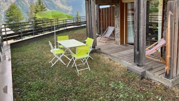 Un terrazzo in legno con tavolo e sedie, con vista su un paesaggio montuoso.