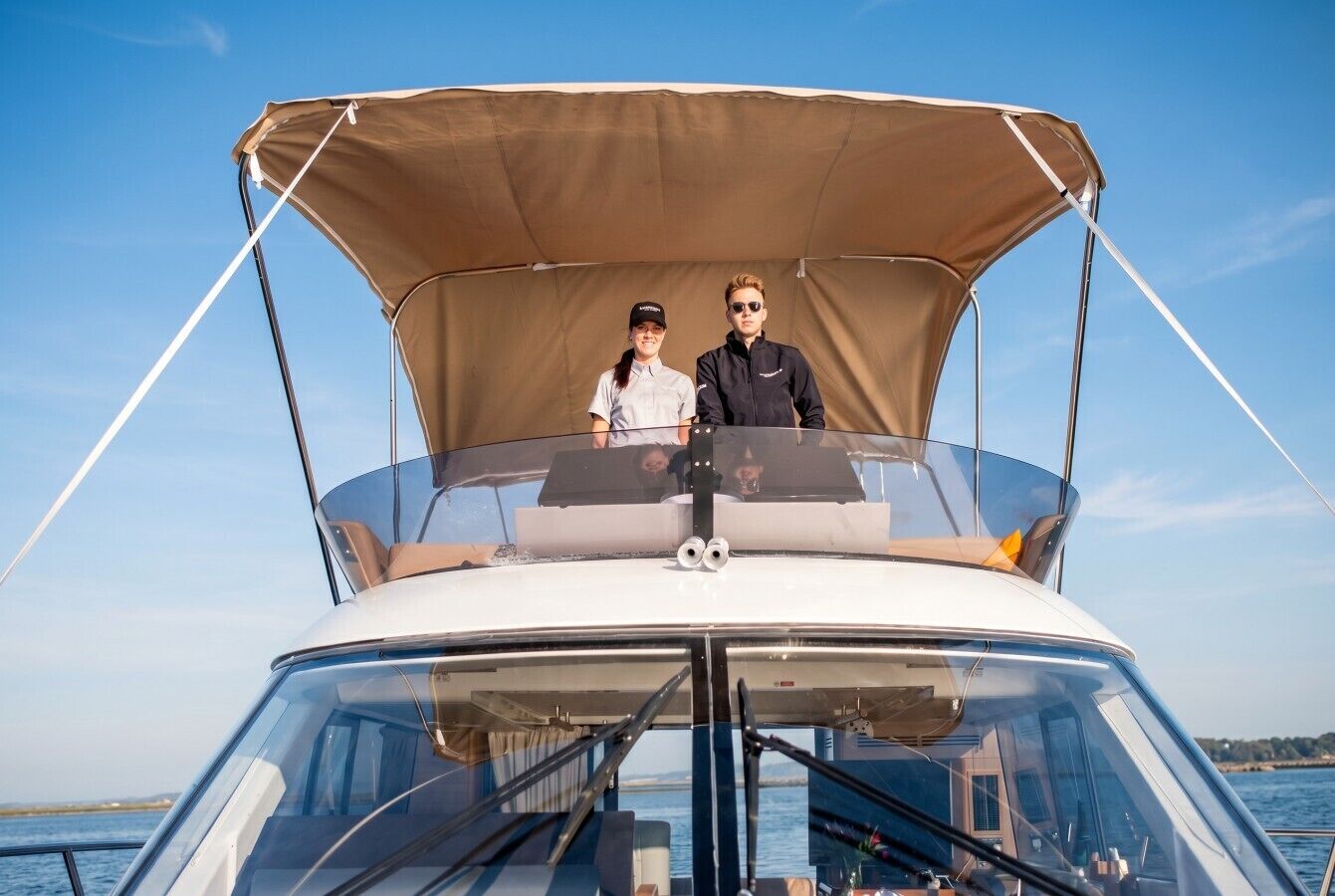 A boat with a canopy, two people on deck, and a clear view of the water.