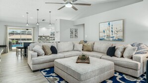 Ein modernes Wohnzimmer mit Ecksofa, Hocker, Deckenventilator, Pendelleuchten und Kunstwerken.