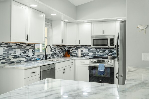 A modern kitchen with white cabinets, a tiled backsplash, stainless steel appliances, and a marble countertop.