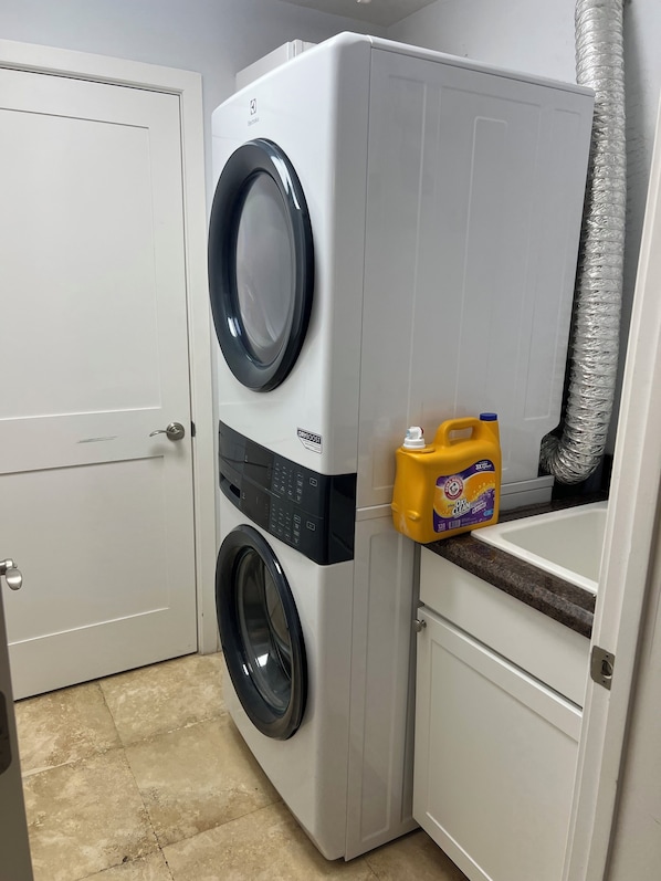 Una lavadora de carga frontal con un panel de control, una botella de detergente y una puerta blanca.