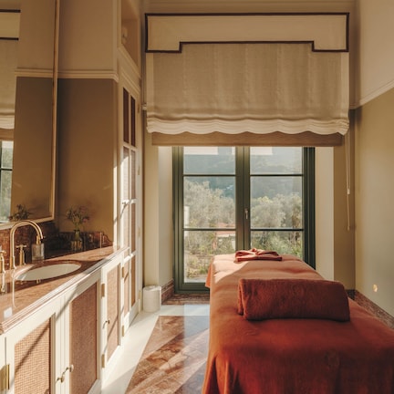 A room with a large window, a bed with a red blanket, a bathroom with a marble sink, and a mirror.