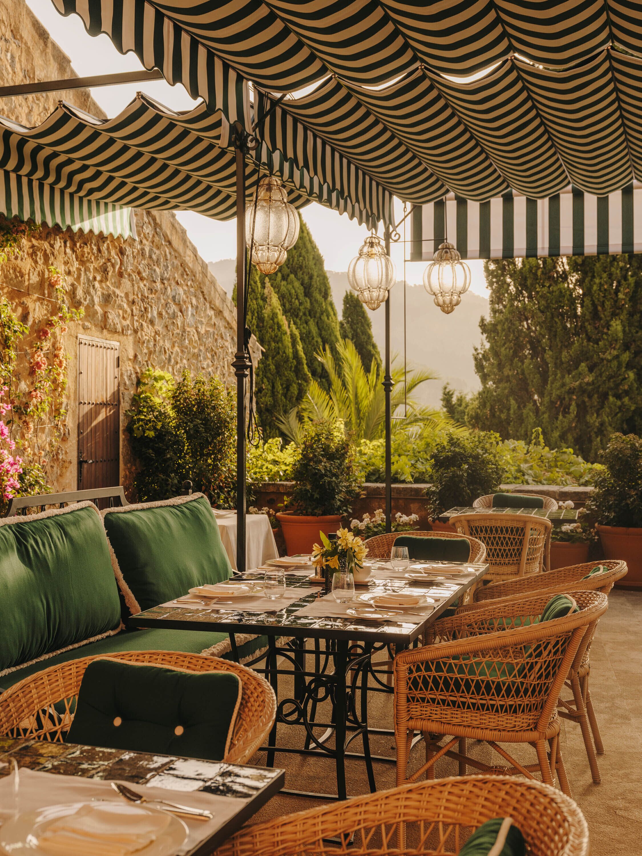 An outdoor dining area with wicker furniture, striped awnings, and hanging lanterns.