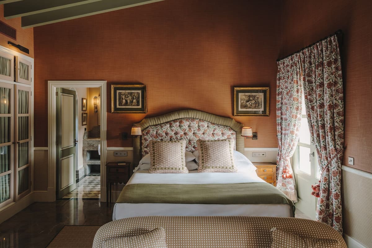 A bedroom with a large bed, a nightstand, a dresser, and a door leading to another room.