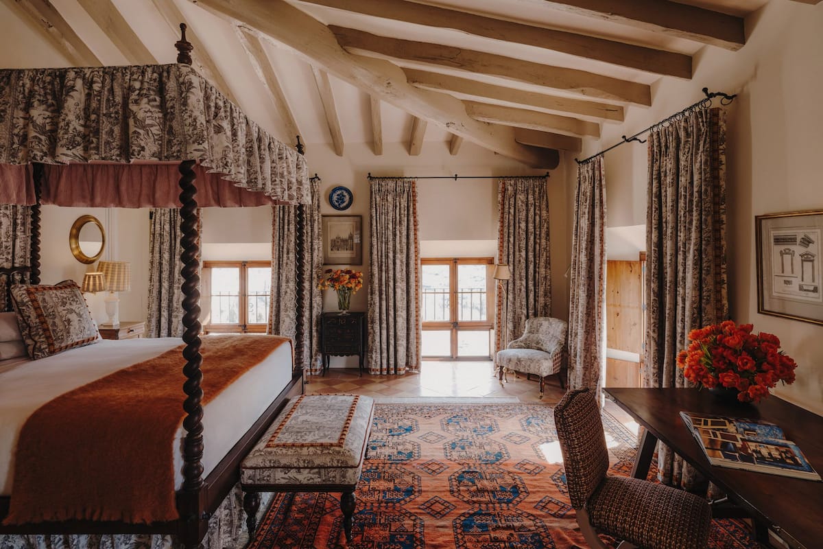 A traditional bedroom with a four-poster bed, a wooden ceiling, and patterned curtains.