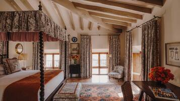 A traditional bedroom with a four-poster bed, a wooden ceiling, and patterned curtains.