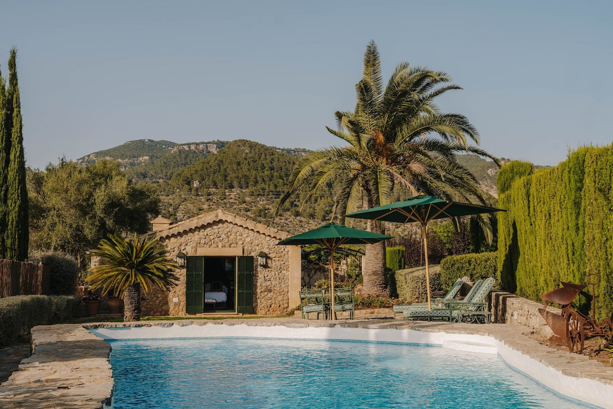 A stone building with a pool, surrounded by palm trees and mountains.