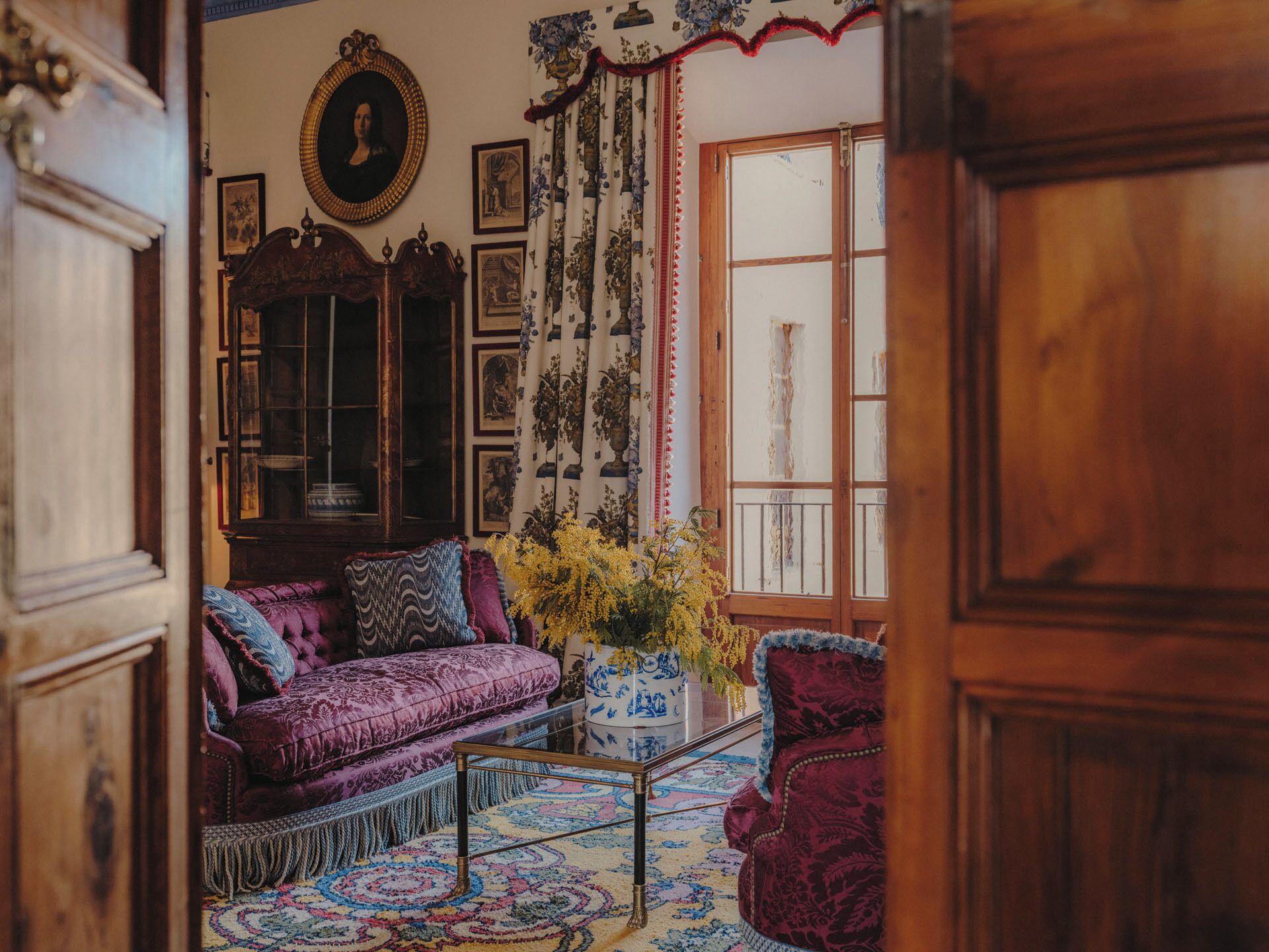 A room with a purple sofa, a wooden cabinet, and a large window with floral curtains.