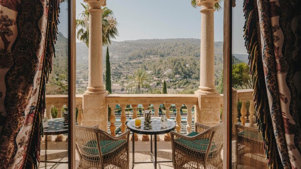 Zona de estar al aire libre con vistas a un paisaje montañoso, que incluye una mesa y sillas bajo un arco de piedra.