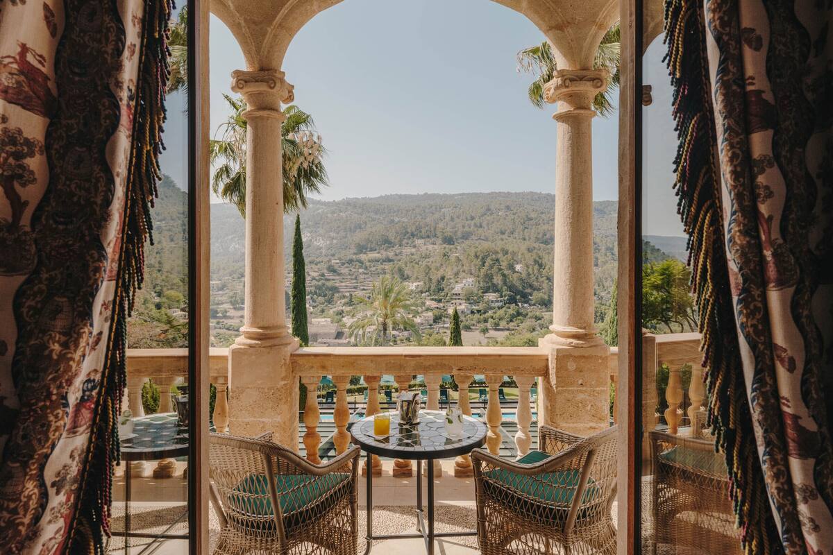 An outdoor seating area with a view of a hilly landscape, featuring a table and chairs under a stone archway.