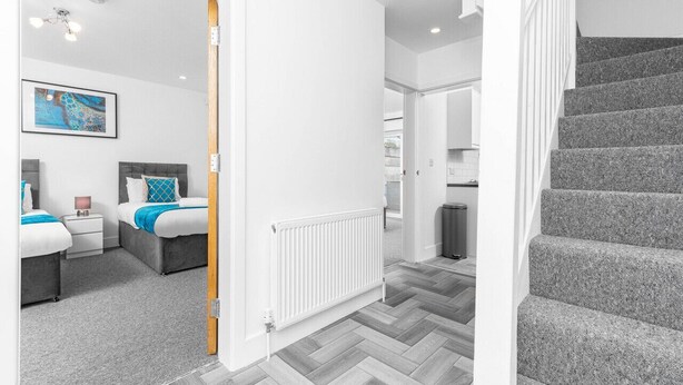 Habitación de hotel moderna con piso de espiga gris, radiador blanco, cabecera gris y una obra de arte enmarcada en la pared.