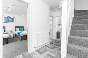 A modern hotel room with a grey herringbone floor, a white radiator, a grey headboard, and a framed artwork on the wall.