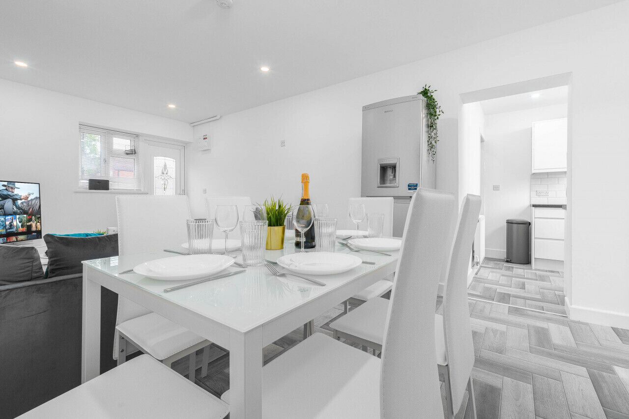 A modern dining area with a white table set for four, a small plant, and a bottle of champagne.