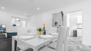 Un comedor moderno con una mesa blanca para cuatro personas, una planta pequeña y una botella de champán.